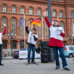 Zwei Frauen und ein Mann erheben die Hände und rufen etwas. Sie stehen vorm Roten Rathaus